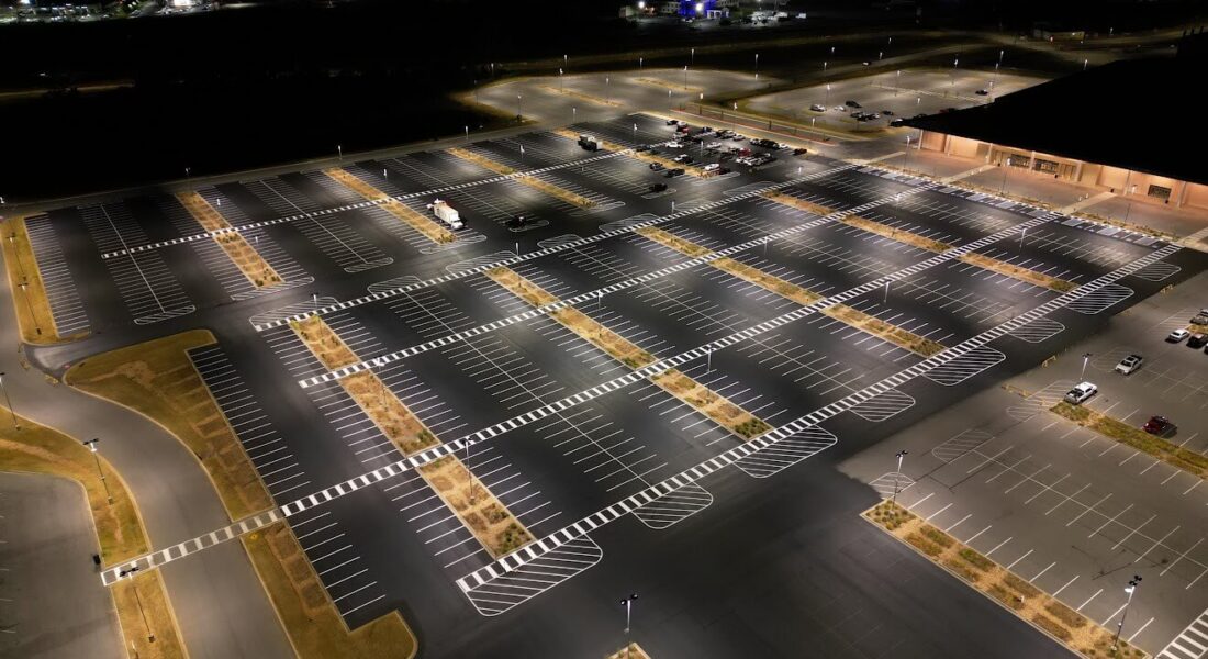 A parking lot at nighttime lit up by lights to show the carefully painted parking spots and directional marking.