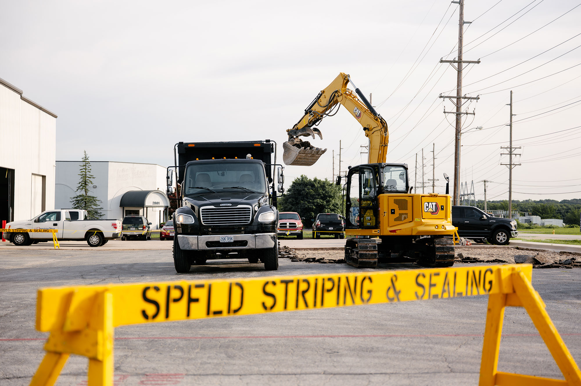 Dump truck and excavator behind SPFLD STRIPING & SEALING barrier.