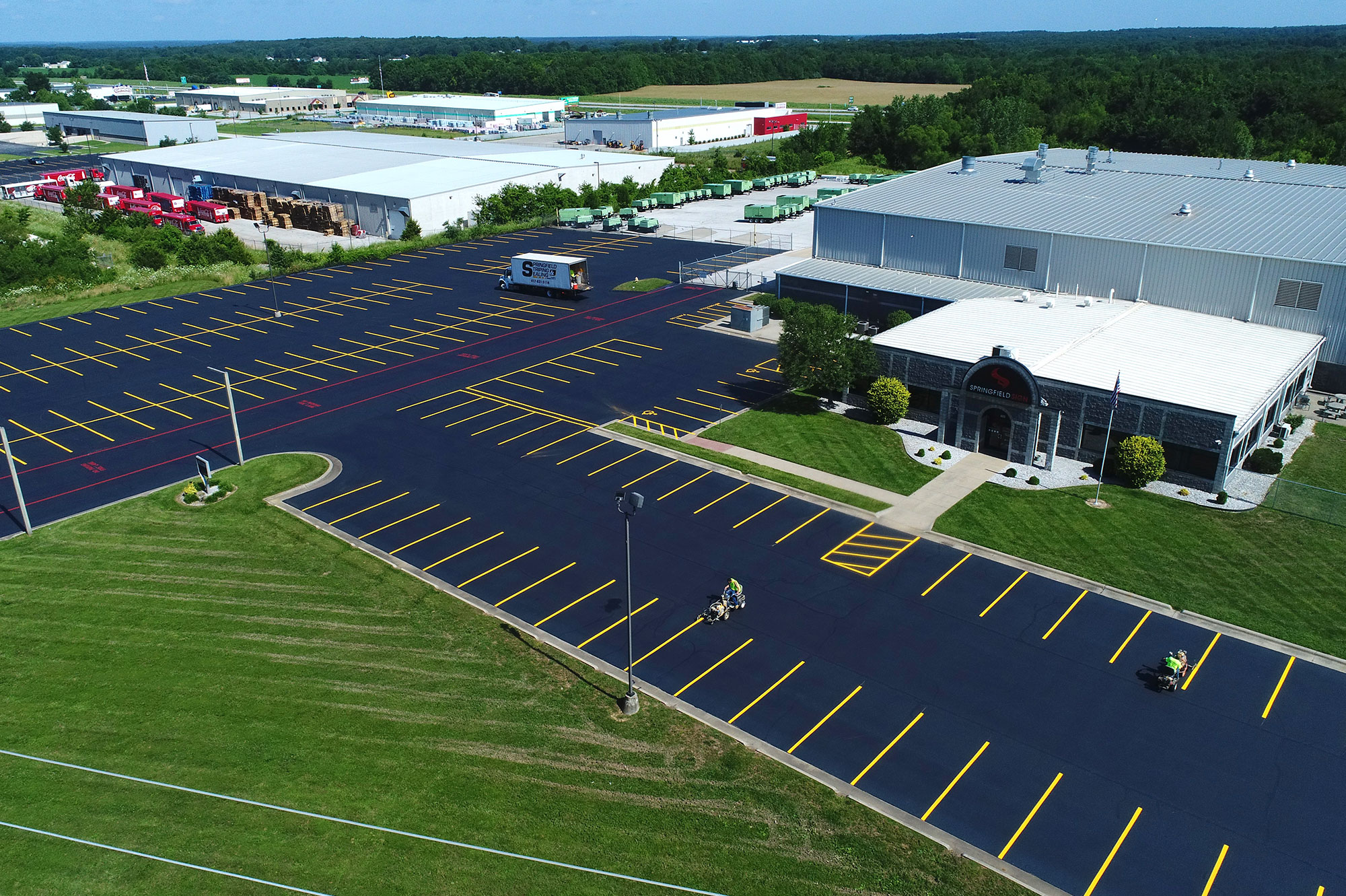 Aerial view of warehouses, new lot, lawns, and trees.